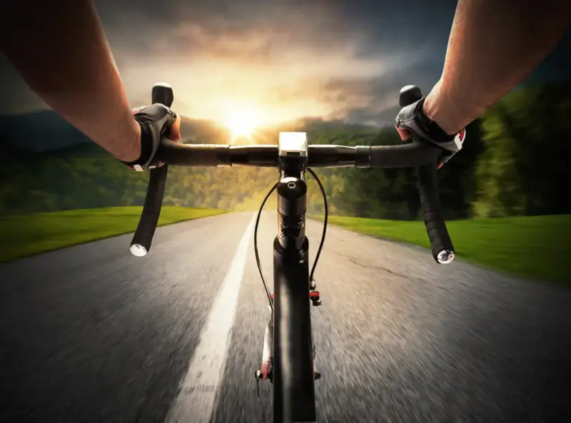 Rowerzysta w rękawiczkach pędzi po asfalcie. Słońce zachodzi, a krajobraz rozmywa się w tle. Ile czasu zajmie mu przejechanie 100 km rowerem?