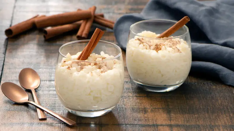 Dos copas de cremoso arroz con leche, espolvoreado con canela y decorado con una rama de canela.