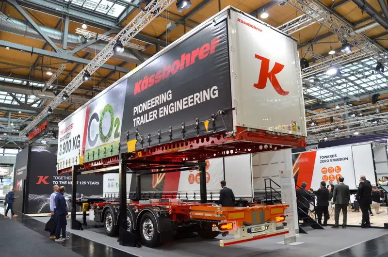 Nowa naczepa Kässbohrer z napisem "Pioneering Trailer Engineering". W tle ludzie zwiedzają targi.