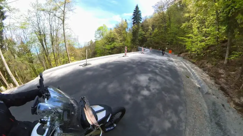 Motocyklista pokonuje zakręty na malowniczej drodze stu zakrętów, otoczonej zielonymi lasami.