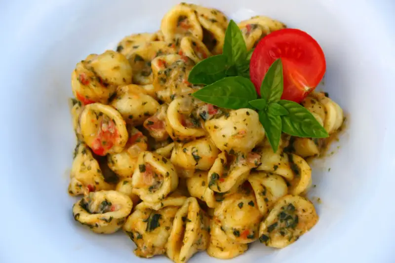 Pyszne makaron orecchiette z sosem pomidorowo-ziołowym, udekorowane listkami bazylii i pomidorem.