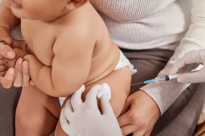 Dziecko otrzymuje szczepienie. Ręka w rękawiczce trzyma strzykawkę, a druga ręka przygotowuje miejsce wkłucia. To ważny moment dla zdrowia, jak w przypadku szczepionki heine medina.