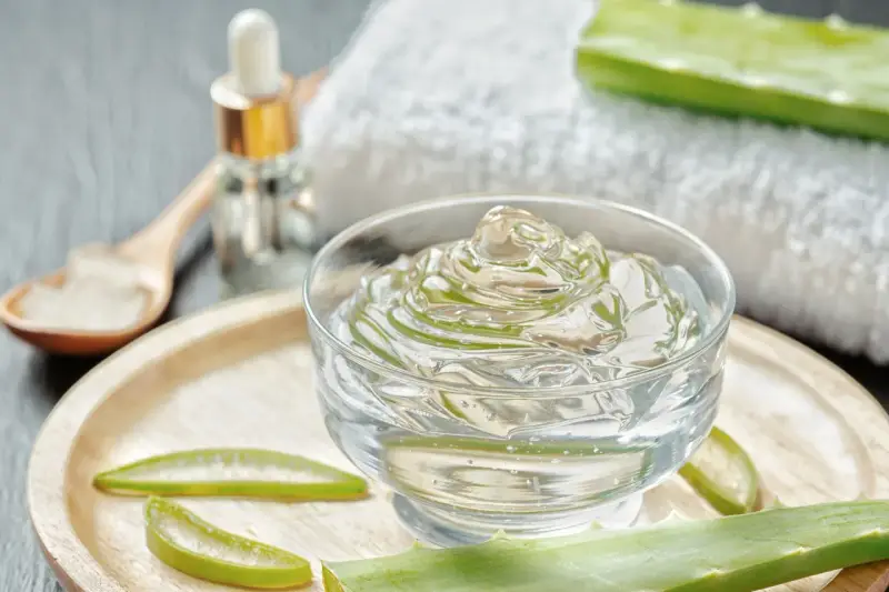 Un bol de gel aloe vera, des tranches d'aloe vera et une cuillère en bois. Découvrez les bienfaits du gel aloe vera pour votre peau.