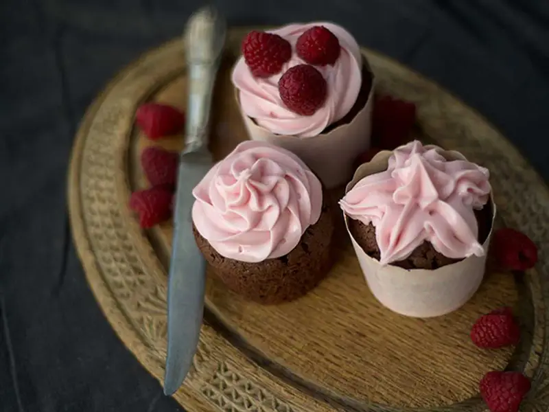 Tre chokladcupcakes med rosa frosting och hallon, redo att avnjutas. Ett perfekt cupcakes recept för alla tillfällen.