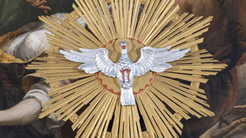 Ein silberner Taube mit ausgebreiteten Flügeln vor einem goldenen Strahlenkranz. Dies symbolisiert den Heiligen Geist und was bedeutet Pfingsten: die Ausgießung des Geistes.