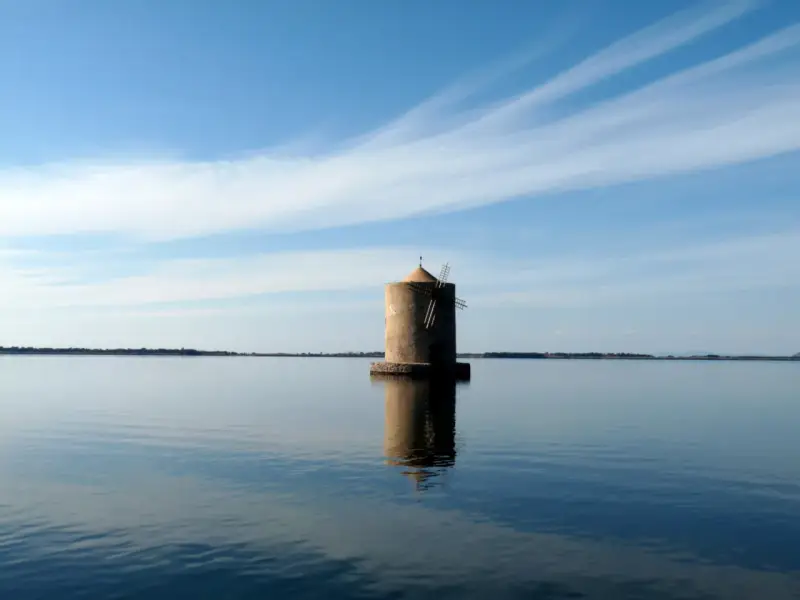 Mulino solitario nella laguna di Orbetello, con cielo azzurro e nuvole sottili.