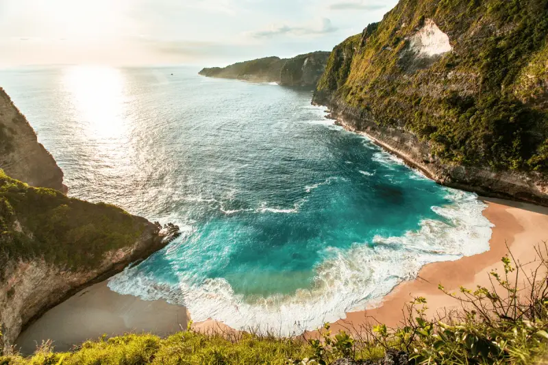 Rajska zatoka z turkusową wodą i piaszczystą plażą, idealna na wakacje na Bali. Klify porośnięte zielenią.