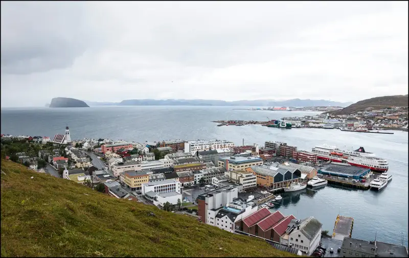 Vy över en stad vid havet med färjor vid kaj. En kyrka med högt torn syns i förgrunden. Detta är Norges nordligaste stad.
