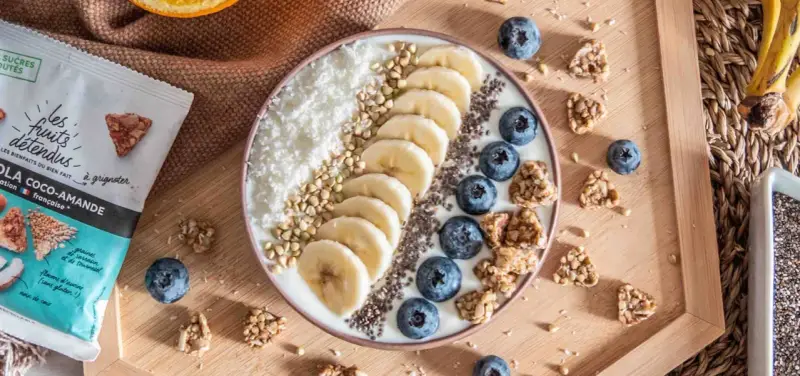 Un bol de smoothie aux bananes, myrtilles, noix de coco râpée et graines de chia, parfait pour un déjeuner au bureau sain et gourmand.