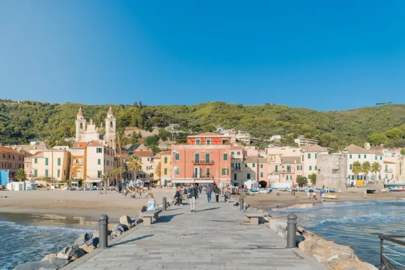 Laigueglia centro storico: case colorate affacciate sulla spiaggia, con una chiesa a due campanili e il mare azzurro.