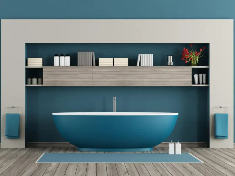 Un moderno bagno azzurro con vasca centrale, mensole piene di libri e flaconi, e due asciugamani blu appesi.