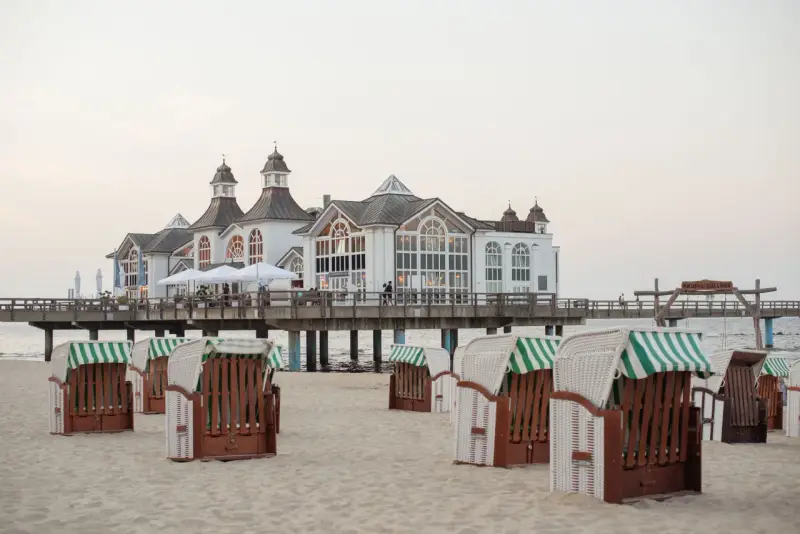 Plaża na wyspie Rugia z charakterystycznymi koszami plażowymi i molo prowadzącym do białego pawilonu.