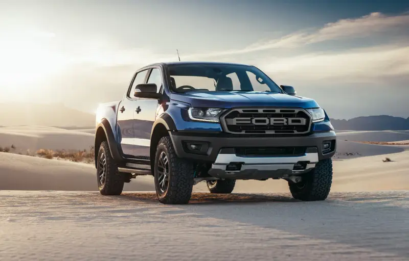Niebieski Ford Ranger Raptor przemierza piaszczyste wydmy o zachodzie słońca.