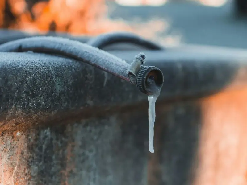 Un tuyau de jardin givré, avec une stalactite de glace tombant du robinet, illustre la nécessité de la protection tuyau en hiver.