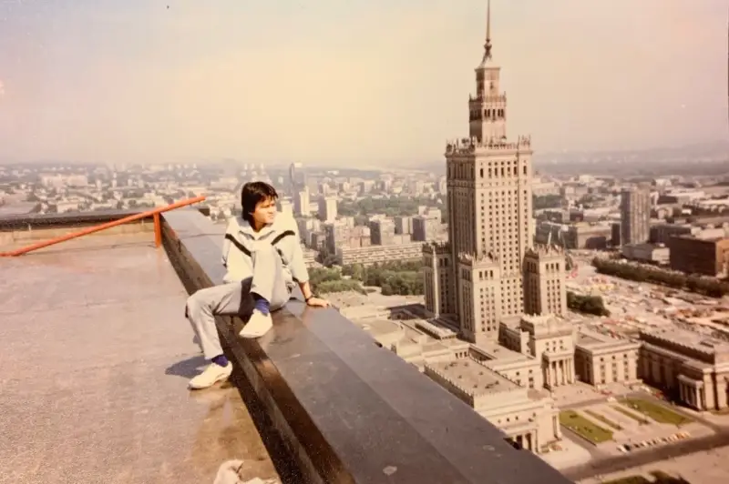 Młody mężczyzna siedzi na dachu, patrząc na panoramę Warszawy. W tle Pałac Kultury i Nauki, który wtedy był najwyższym budynkiem, zanim powstał Marriott.