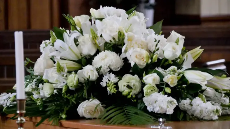 Un arreglo floral blanco sobre un ataúd, con lirios, rosas y otras flores. Estas flores para difuntos simbolizan paz y pureza en el adiós.