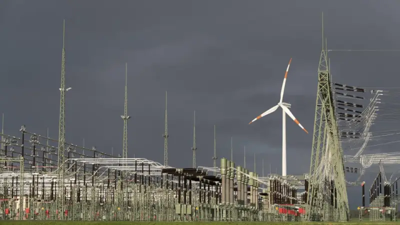 Ein Windrad und eine weitläufige Schaltanlage symbolisieren den Ausbau des Stromnetzes für erneuerbare Energien.
