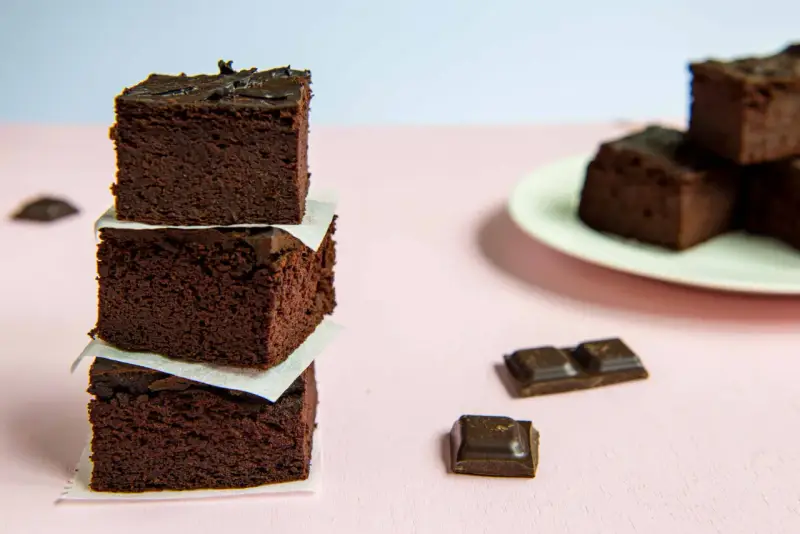 Ciemne, wilgotne brownie z fasoli, ułożone w wieżę, obok kawałków czekolady.