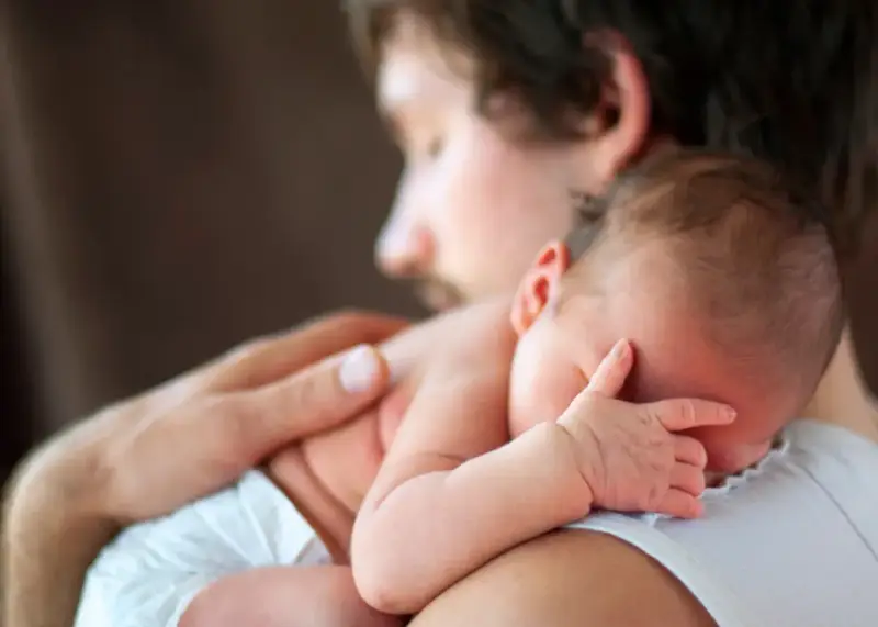 Padre abbraccia neonato. Osservare attentamente i sintomi autismo nel neonato di 3 mesi, come la mancanza di contatto visivo o risposte emotive atipiche.