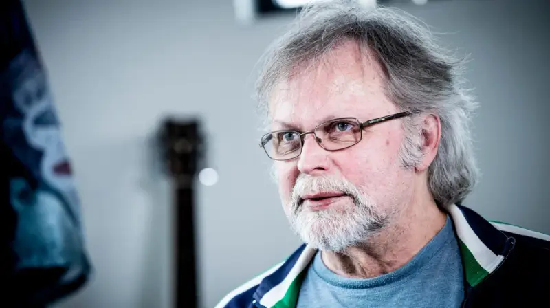 Clark Olofsson idag, med grått hår, skägg och glasögon, blickar mot betraktaren.