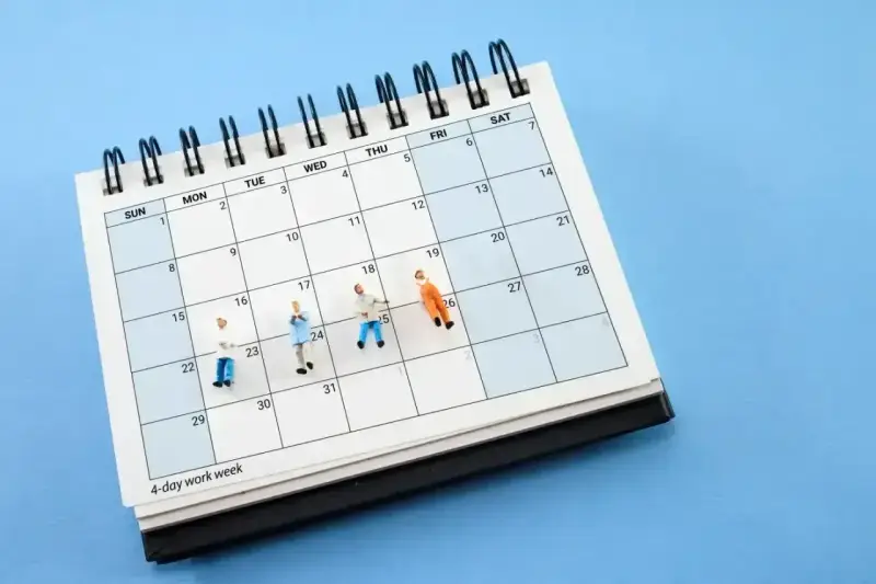 Miniaturki ludzi na kalendarzu z napisem "4-day work week". To karta nauczyciela zmian, która pokazuje, jak można zaplanować krótszy tydzień pracy.