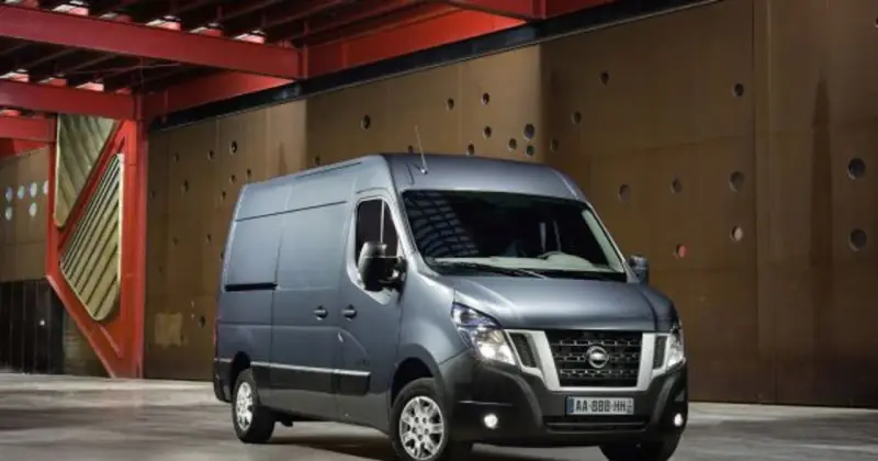 Szary Nissan NV400 stoi przed brązową, perforowaną ścianą w industrialnym wnętrzu.