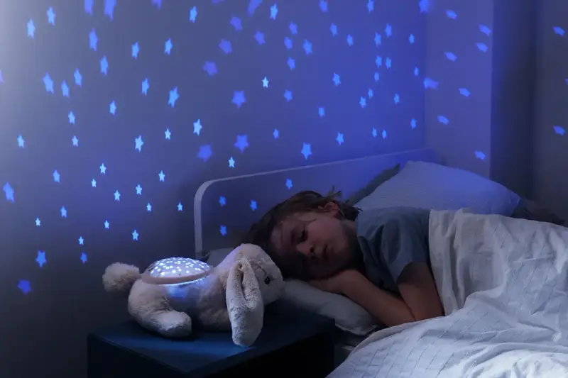 Uroczy króliczek z projektorem dla niemowlaka rzuca na ścianę niebieskie gwiazdki, tworząc magiczną atmosferę do snu.