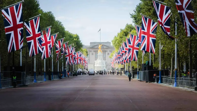 Allée bordée de drapeaux britanniques menant à un palais, avec des arbres et des gardes.