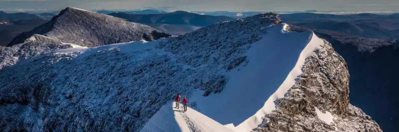 Två vandrare på en snöig bergskam, redo att bestiga Kebnekaise. Vacker utsikt över fjällen.