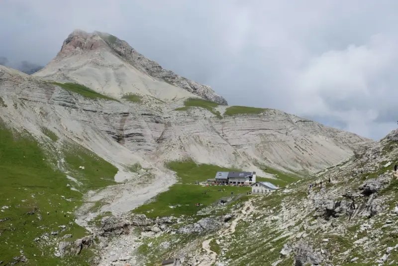 Rifugio alpino con escursionisti e gregge in un paesaggio montano mozzafiato, vicino a Passo Val Gardena.