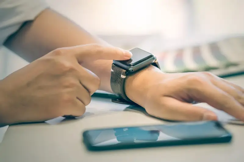 Dłoń z zegarkiem na nadgarstku, palec dotyka ekranu, pokazując jak włączyć bluetooth w smartwatch.