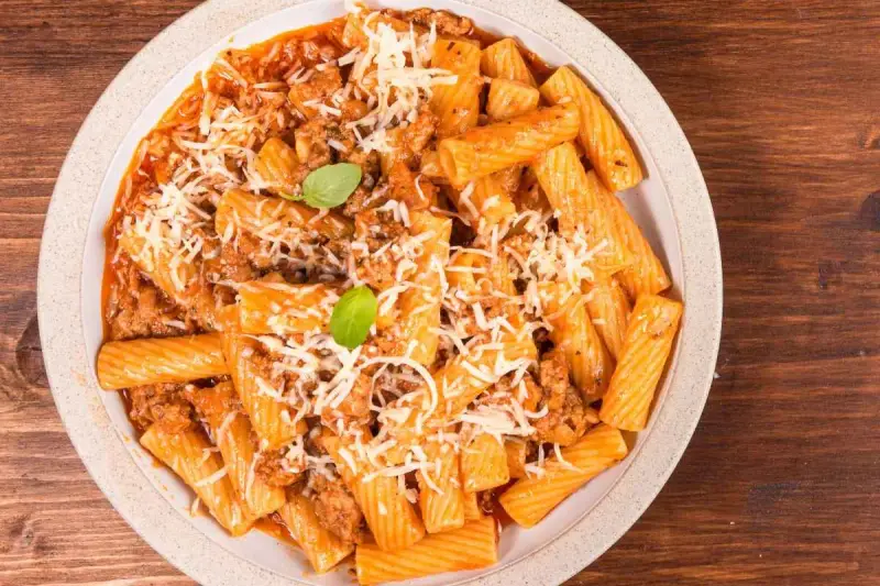 Un piatto invitante di pasta alla zozzona, con rigatoni conditi con un ricco ragù e abbondante parmigiano grattugiato, guarnito con basilico fresco.