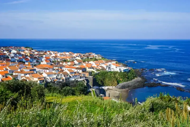 Malownicze miasteczko na wybrzeżu Portugalii, z białymi domami i pomarańczowymi dachami, nad błękitnym oceanem. Ceny wakacji w Portugalii mogą być zaskakująco przystępne.