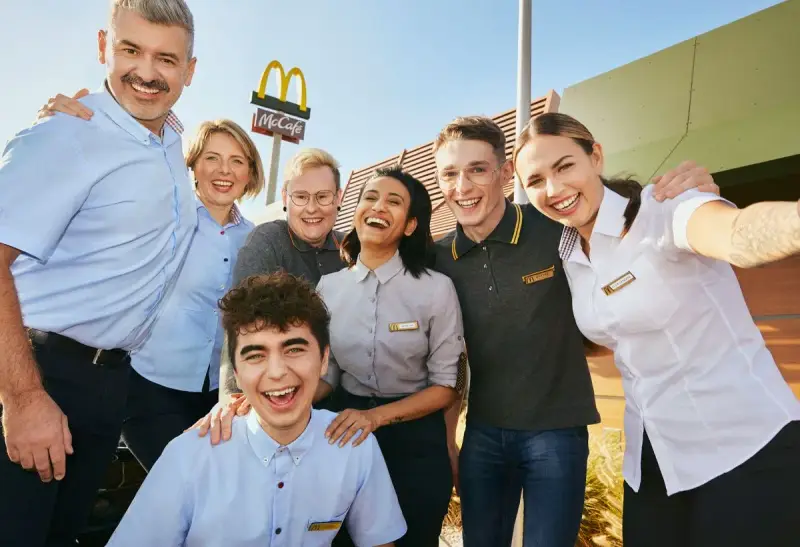 Uśmiechnięty zespół McDonald's, gotowy do pracy. W tle logo McCafe.