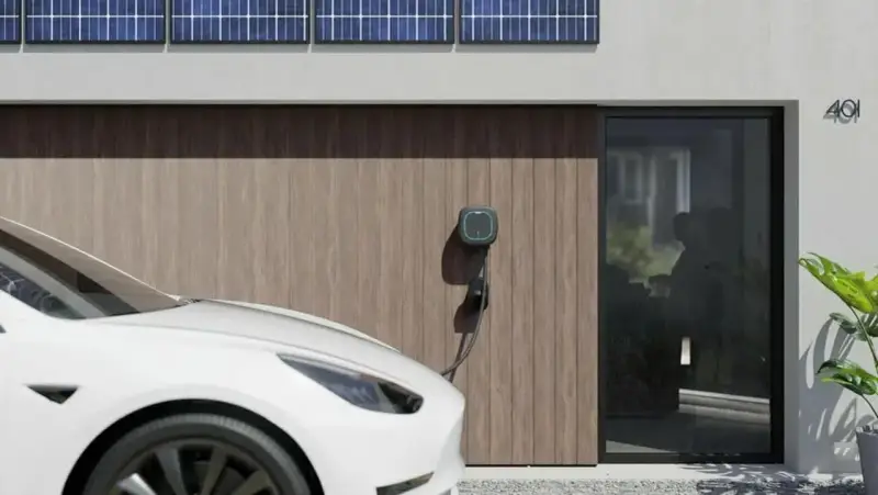 Białe auto elektryczne (BEV) podłączone do ładowarki przy nowoczesnym domu z panelami słonecznymi.