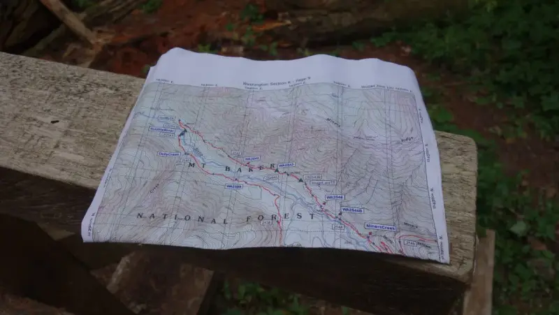 Mapa szlaku grzbietu pacyficznego z zaznaczonymi punktami i rzekami, leżąca na drewnianej ławce.