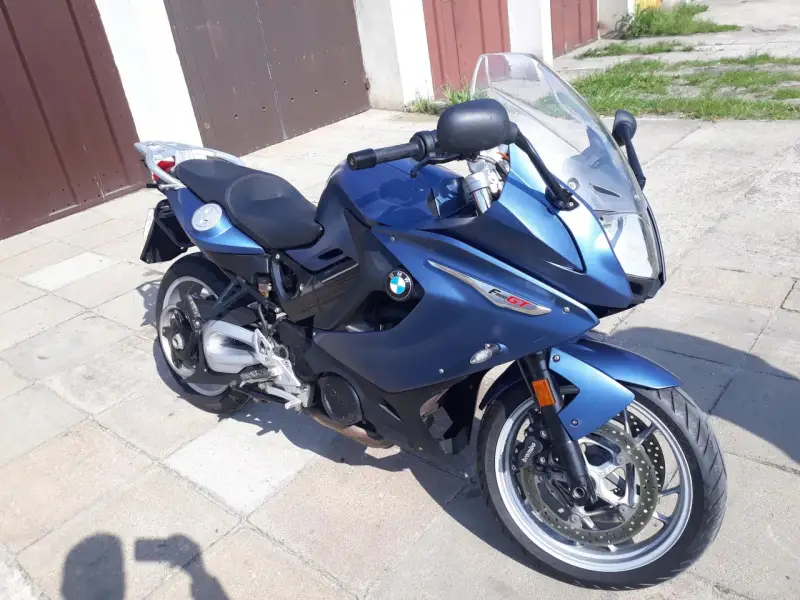 Błękitny motocykl BMW F800 GT stoi na chodniku przed garażem.