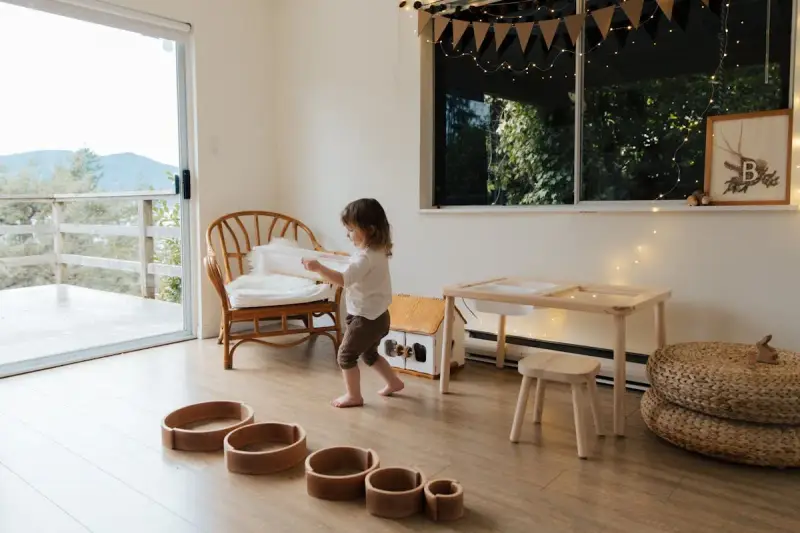 Bambina gioca in una stanza giochi in casa, tra sedie di vimini, tavolino e cesti.