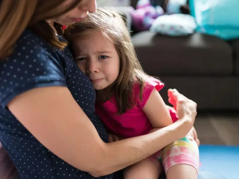Mała dziewczynka płacze, wtulona w mamę. To właśnie parenting – trudne chwile i bezwarunkowa miłość.