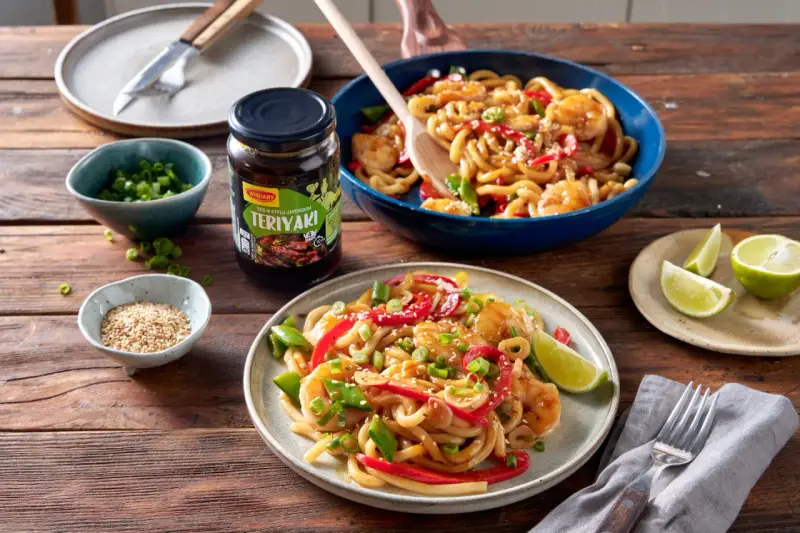 Krewetki z makaronem w sosie teriyaki, podane na talerzu z dodatkami.