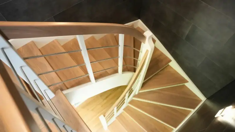 Drewniane schody kacze z białymi balustradami i metalowymi poręczami, prowadzące w dół.