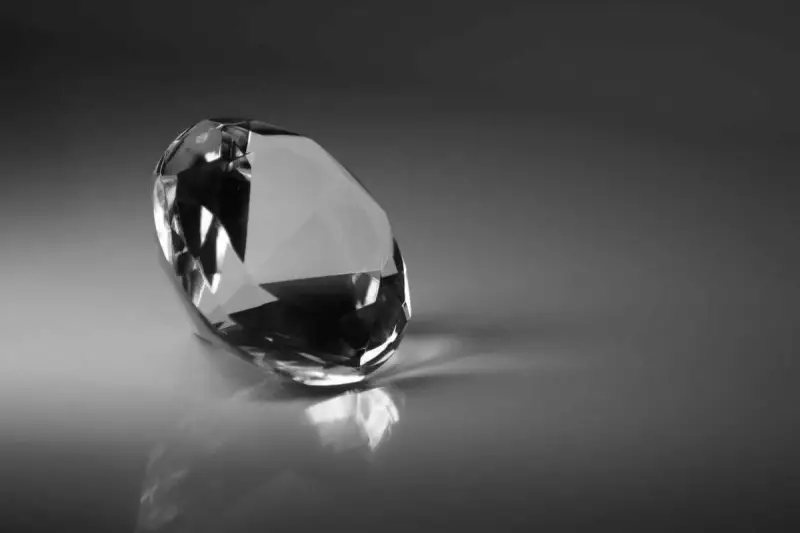 Un diamante sfaccettato riflette la luce su una superficie lucida. Il suo fascino misterioso evoca il significato dei diamanti neri: forza e resilienza.