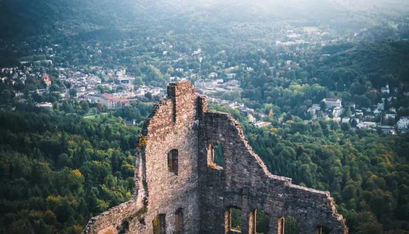 Ruinen einer Burg mit Blick auf eine Stadt und bewaldete Hügel.