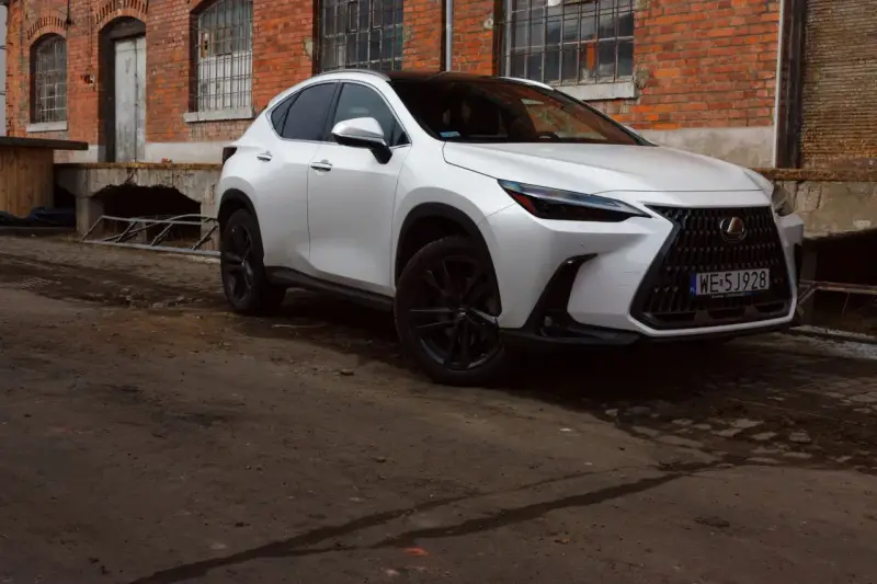 Biały Lexus 350h z czarnymi felgami stoi przed starą ceglaną budowką.