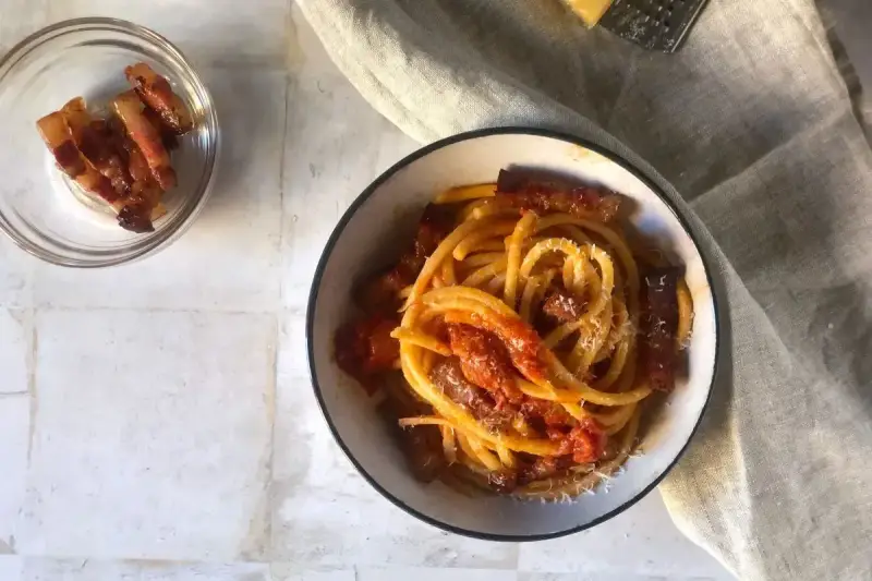 Un piatto invitante di bucatini all'amatriciana, con guanciale croccante e una salsa rossa saporita, spolverato di formaggio grattugiato.