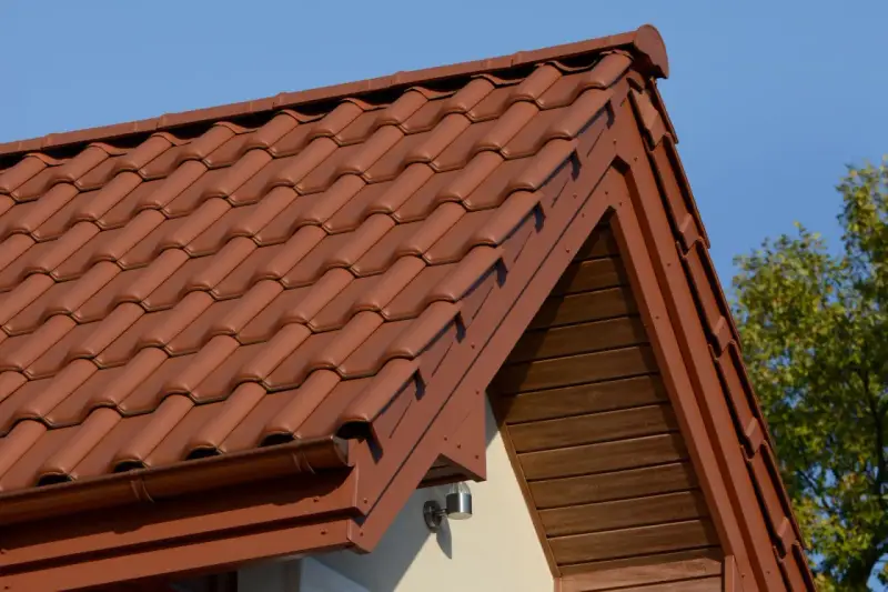 Brązowa, lekka konstrukcja dachu z dachówki ceramicznej, z widocznym okapem i drewnianą podbitką.