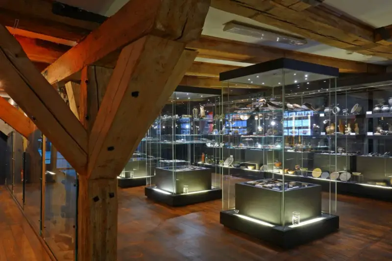Wnętrze muzeum z zabytkowymi belkami i przeszklonymi gablotami pełnymi artefaktów. Może tu jest też błękitny baranek?