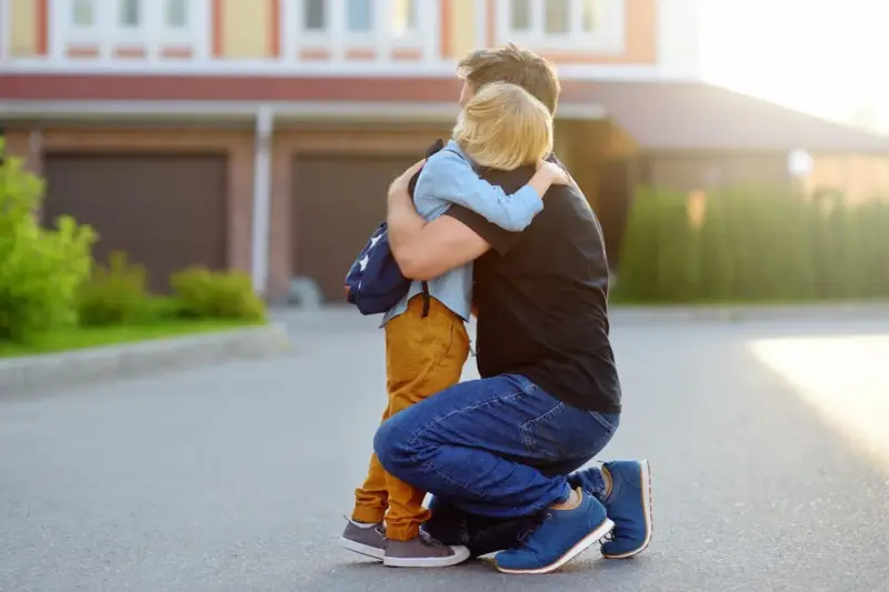 Vater umarmt seinen Sohn mit Rucksack. Ein guter Schulstart nach den Ferien beginnt mit einer liebevollen Umarmung.