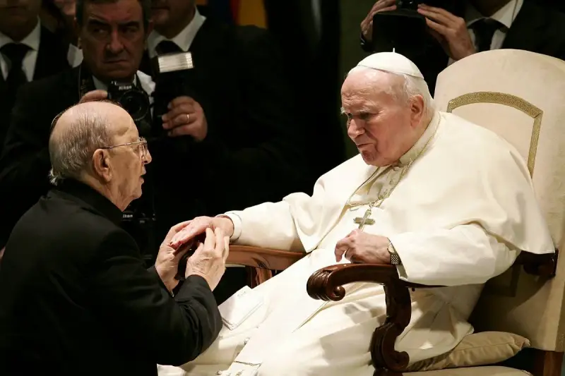 Papież Jan Paweł II w białej szacie, klęczący mężczyzna w czerni. W tle widać fotografów. To obraz duchowej siły, jakiej doświadczają legiony Chrystusa.