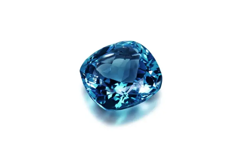 A cushion-cut blue gemstone, likely sapphire, what is September's birthstone, sparkles against a white background.